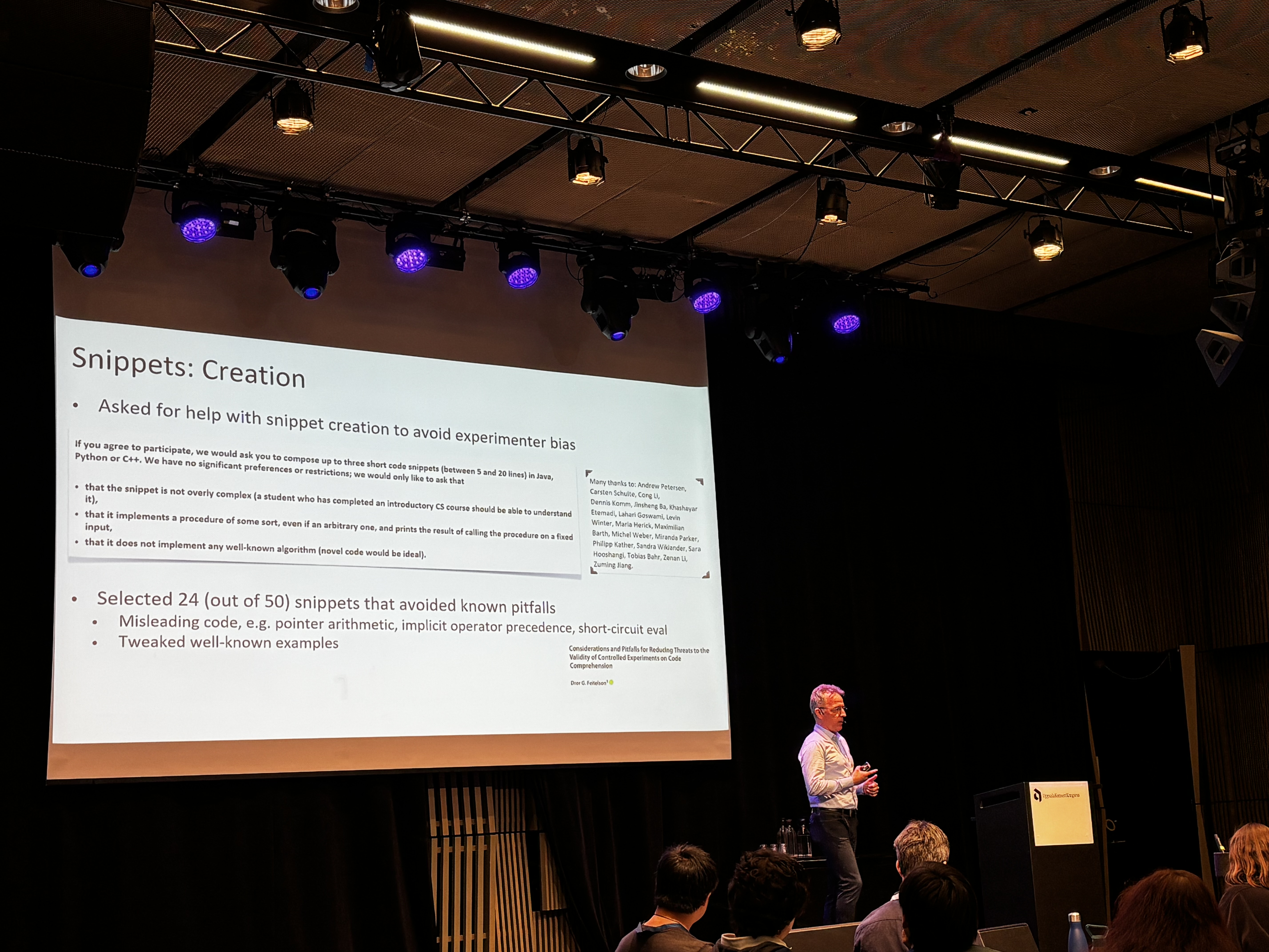Jan Vahrenhold presenting their work next to a large projector screen. On the slide is a description of the process of sampling code snippets for the study, as well as a list of names for the experts who contributed.