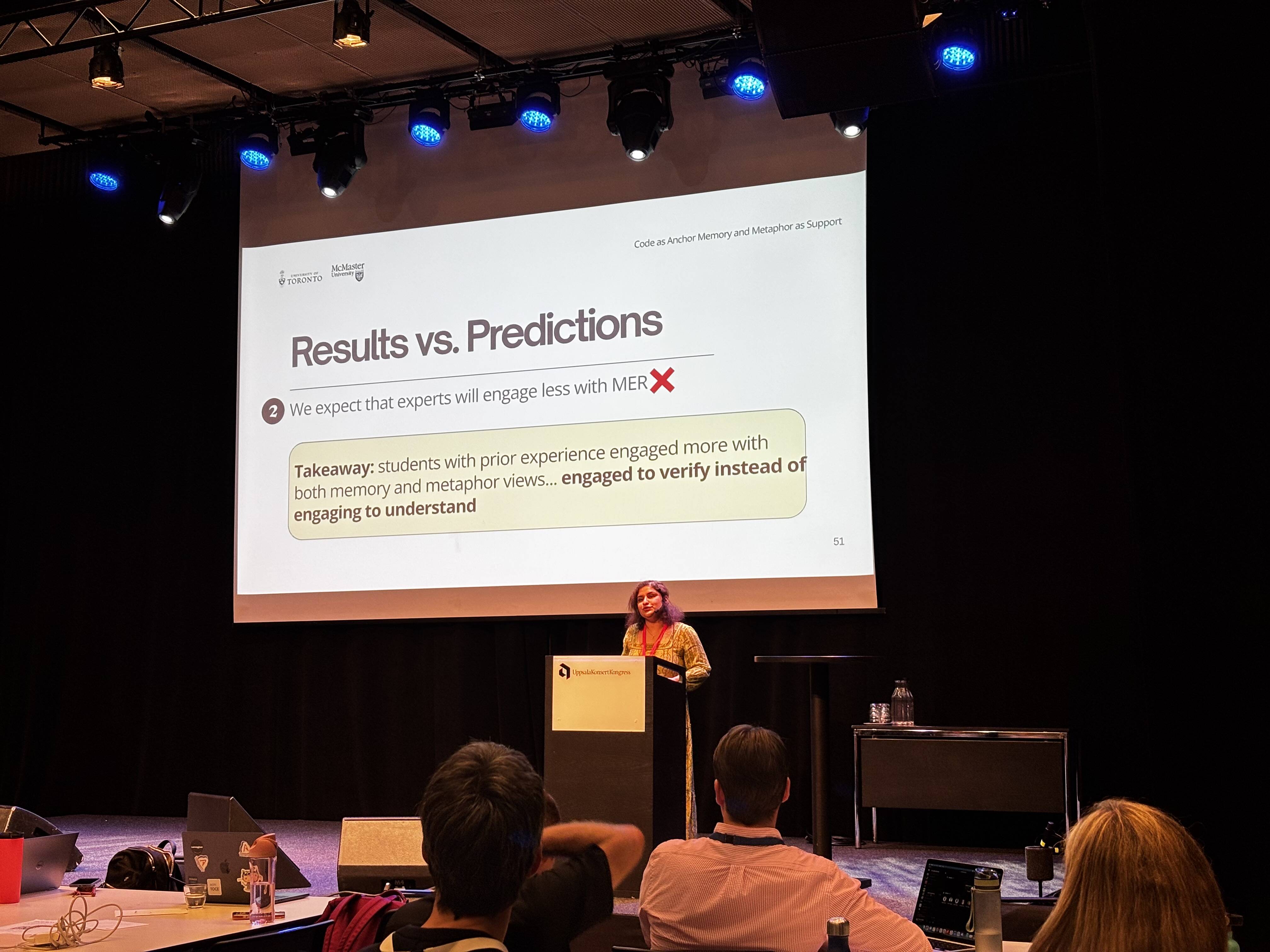Naaz Sibia at a lectern, discussing their predictions versus their actual results, as well as the associated take-aways.