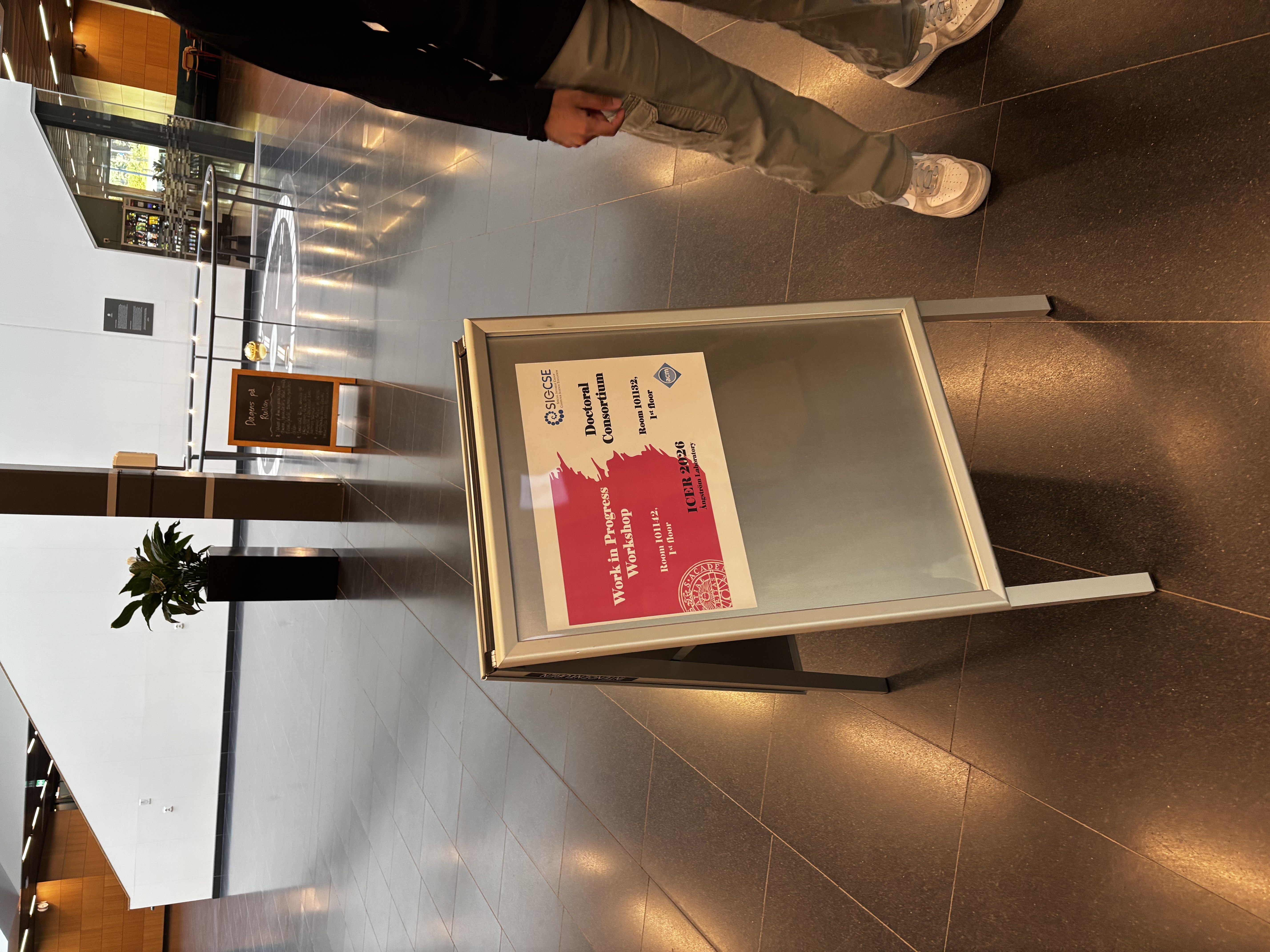 A board with a sign on it indicating the room numbers for the work in progress workshop and the doctoral consortium.